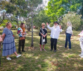 Group of people gathered in bush land with a man gesturing and explaining something to the group