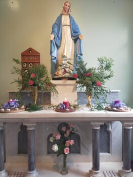 Altar in a Catholic church featuring a statue of Mary and floral arrangements