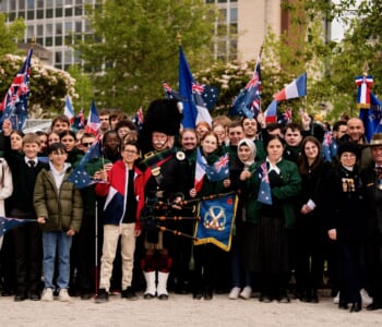 Large group of people smiling waving French and Australian flags some are in civilian clothes others in military uniform