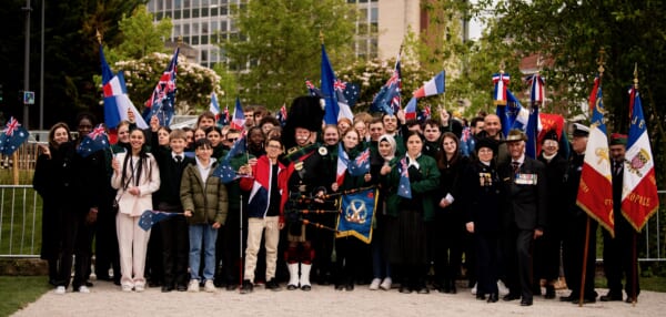 Large group of people smiling waving French and Australian flags some are in civilian clothes others in military uniform