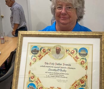 Woman holding framed Papal Blessing gifted to her for 50 years of working for the Catholic Church.