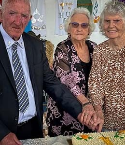 Three elderly people cutting a cake
