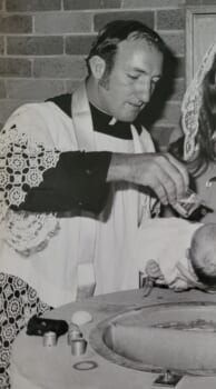 Black and white photo of a Catholic priest baptising a child
