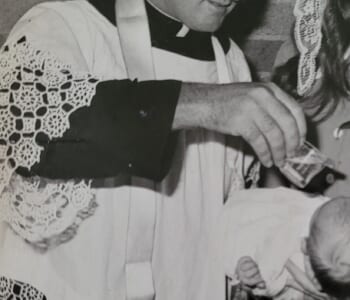 Black and white photo of a Catholic priest baptising a child