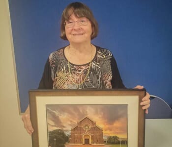 Woman holding framed photo of church gifted to her upon retirement