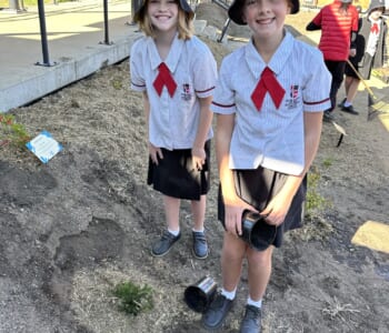 Two girls in school uniform planting a shrub in a new garden