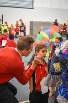 An adult is bending over to paint a heart on a boys face.