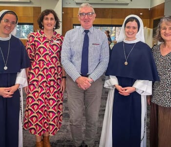 Group of people posed smiling, two are Catholic nuns dressed in blue and white habits