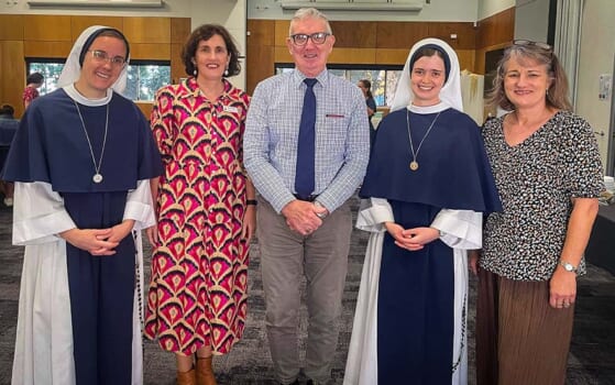 Group of people posed smiling, two are Catholic nuns dressed in blue and white habits