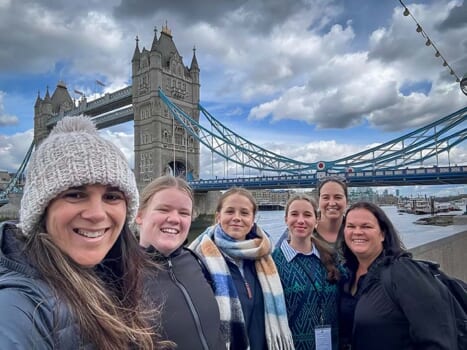 Group of smiling people posed in front of the London Bridge, London