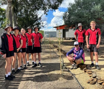 Group of students in school uniform planting trees their teacher is sitting next to the tree.