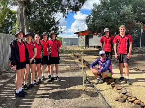 Group of students in school uniform planting trees their teacher is sitting next to the tree.