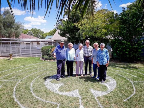 A group of people posed together smiling in the sun in a back yard garden