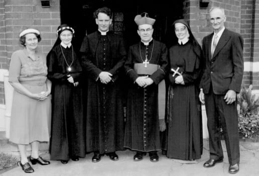 A black and white photo of people posed smiling, some are Cathoilc clergy, some are nuns and others are regular people in civilian clothes