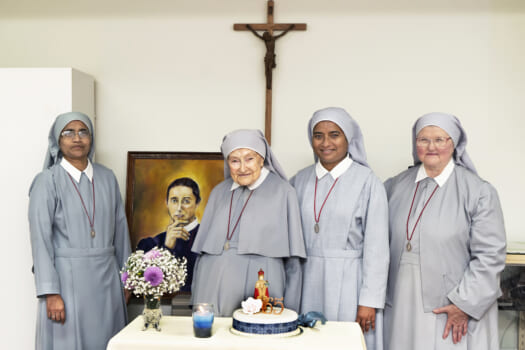 A group of nuns in grey habits pose smiling with a cake