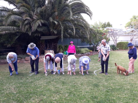 A group of people are following string as a guide to mark out a labryinth outline in the grass in a back yard.