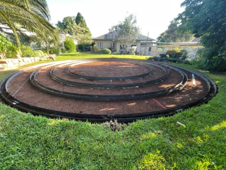 Metal rings laying in a shallow hole dug in a back yard will form the template for pouring concrete to form a labyrinth garden feature.