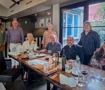 Group of smiling people gathered around a table after enjoying a meal together.